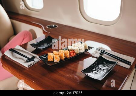 7/8-Ansicht der Frau in der Nähe von lecker Sushi sitzen in Private Jet Stockfoto