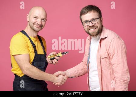 Dankbar Client macht einen Handshake Geste mit einem Arbeitnehmer, der einen guten Job hat, Männer schauen und lächeln in die Kamera. Stockfoto