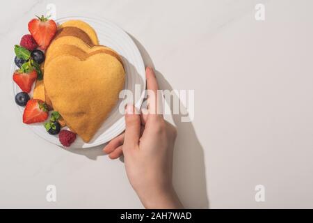 7/8-Ansicht von Frau Halteplatte mit herzförmigen Pfannkuchen und leckere Beeren auf Platte auf weißem Hintergrund Stockfoto