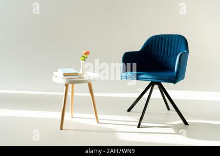 Blau moderne Sessel und Couchtisch mit Blume in der Vase und Bücher auf grauem Hintergrund Stockfoto