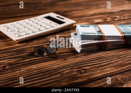 Selektiver Fokus der Weißen Taschenrechner in der Nähe von russisches Geld und Münzen am Holztisch Stockfoto