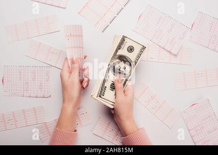 7/8-Ansicht von Frau mit Dollar Banknoten und Lottery Ticket in der Nähe verstreut Lotterie Karten auf weißen Tisch Stockfoto