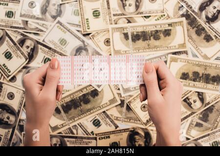 7/8-Ansicht von Frau mit Lottoschein mit markierten Zahlen in der Nähe verstreut Dollar Banknoten Stockfoto