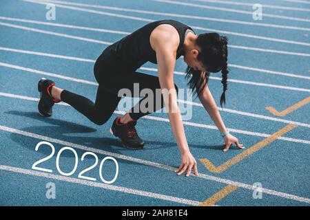 Junge Sportlerin in Start postulieren auf der Laufstrecke in der Nähe von 2020 Schriftzug Stockfoto