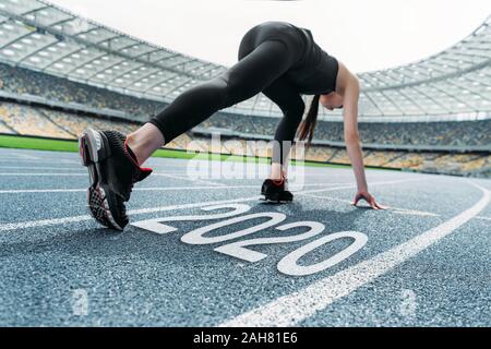 Junge Sportlerin in Start postulieren auf der Laufstrecke in der Nähe von 2020 Schriftzug Stockfoto
