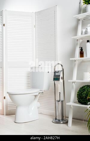 Innenraum der Weißen modernes Bad mit WC Schüssel in der Nähe von Folding Screen, Rack und Anlagen Stockfoto