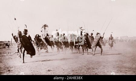 Sudan, gedruckte Überschrift liest: hulluk Krieger, Upper Nile. Durch G N Morhig, die deutsche Apotheke, Khartum veröffentlicht. Copyright 192'. Eine Gruppe von shilluk Krieger kostenlos entlang einer staubigen Ebene, die Schilde und Speere, [c 1906]. 2003/222/1/2/90. Stockfoto