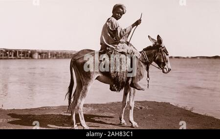 Sudan, gedruckten Bildunterschrift lautet: "Ein Esel, der Junge, Khartum. Durch G N Morhig, die deutsche Apotheke, Khartum veröffentlicht. Copyright 121'. Porträt eines sudanesischen Junge, rittlings auf einem genutzt Esel neben einem Nebenfluss des Nil, [c 1906]. 2003/222/1/1/53. Stockfoto
