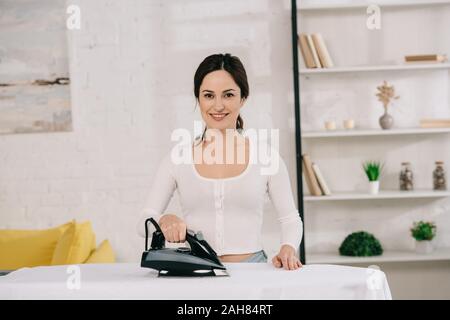 Freundliche Hausfrau Lächeln auf die Kamera beim Bügeln auf dem Bügelbrett Stockfoto