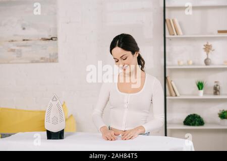 Gerne Hausfrau Lächeln beim Stehen in der Nähe von Bügelbrett Stockfoto