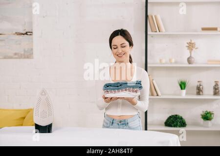 Gerne Hausfrau Holding gebügelte Kleidung beim Stehen in der Nähe von Bügelbrett Stockfoto