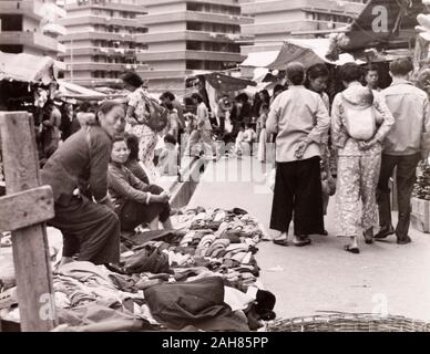 Hong Kong, Kleidung Markt in Hongkong KongStreet Händler ihre Waren an einem langen Kleidung Markt. Hinter ihnen sind mehrere mehrstöckigen Umsiedlung Blöcke, die alle über Kowloon von der britischen Regierung gebaut wurden re-Haus 70.000 Menschen nach Brand zerstört eine überfüllte Hausbesetzer Siedlung im Jahre 1953. Originalmanuskript Bildunterschrift: Alte Kleidung Markt außerhalb einer der großen Umsiedlung Gebäude, 1963. 2005/010/1/11/38. Stockfoto