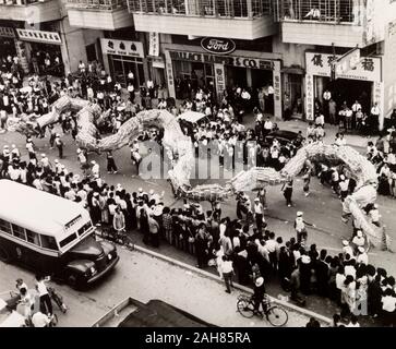 Hong Kong, Dragon dance für den Tin Hau FestivalA chinesischer Drachentanz schlängelt sich durch Massen von Zuschauern auf einer Straße in Yuen Long während der Feierlichkeiten für das Taoistische Tin Hau Festival. Originalmanuskript Bildunterschrift: Inmitten von sich überschneidenden Zimbeln und Bass kommt ein 100 ft. Drachen tanzen und Herunterziehen der Straße. Shop Inhaber und Schüler, Hausfrauen und Arbeiter alle stop was Sie tun; auch der Bus hat auf der einen Seite der Straße zu ziehen, die Parade auf der Main Street von Youen Lange während der Tin Hau Festival, 1963 zu beobachten. 2005/010/1/11/33. Stockfoto