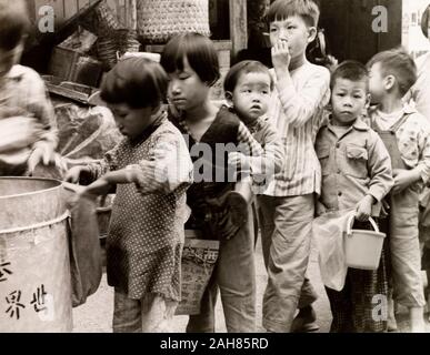 Hong Kong, Kinder Queuing für Lebensmittel, Hong KongCity Kinder queue mit Containern, warten Lebensmittelrationen von einer wohltätigen Organisation zu erhalten. Originalmanuskript Bildunterschrift: Schülerinnen und Schüler erhalten, präsentiert von Lebensmitteln von einer wohltätigen Organisation, 1963. 2005/010/1/11/41. Stockfoto