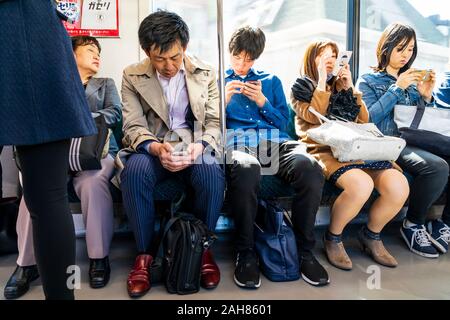 Vier japanische Pendler im Zug in einer Reihe sitzen gegen Wagen Fenster Alles über Handys. Innenraum der Waggon. Stockfoto