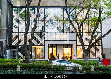 Über street view der Britischen modische Burberry Store unter der Omotesando Avenue. Blaue Stunde, Gebäude beleuchtet. Zwei Bäume vor. Stockfoto