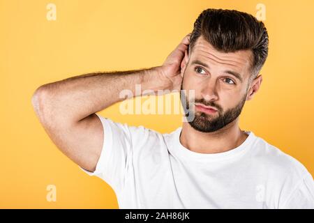 Nachdenklicher Mann im weißen T-Shirt kratzen Kopf auf gelb isoliert Stockfoto