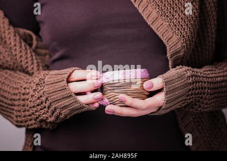Schöne weibliche Hand, die eine braune Ton Textur Cup. Maniküre mit rosa Nagellack. Gemütliche Konzept Stockfoto