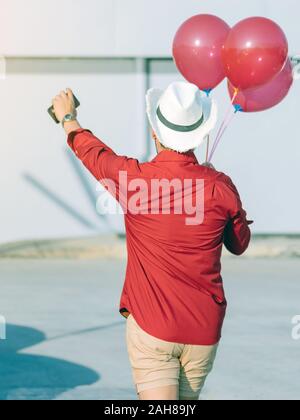 Rückansicht des homosexuellen Mann im roten Hemd mit roten Ballons vom Parkplatz der Partei am Nachmittag zu verbinden. Stockfoto