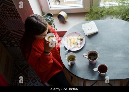 Blonde Mädchen mit langen Haaren in einem roten Pullover am Esstisch sitzen Stockfoto