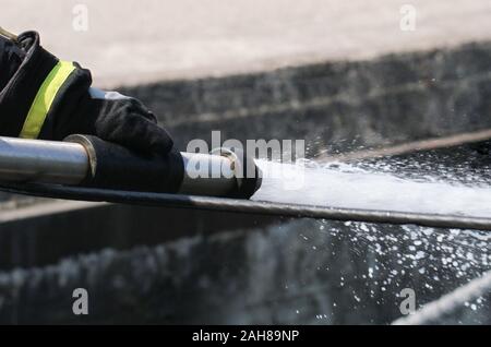 Feuerwehrmann spritzen das Wasser aus dem Schlauch. Stockfoto