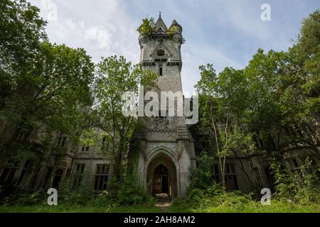 Symmetrische Weitwinkelansicht eines alten verlassenen Burg, mit einem Uhrturm in der Mitte, umgeben von Bäumen und Vegetation Stockfoto