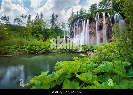 Niedriger Winkel Blick auf einen ikonischen kroatischen Wasserfall, umgeben von grüner Vegetation und unter einem blauen Himmel mit geschwollenen Wolken, im Naturpark Plitvice Stockfoto