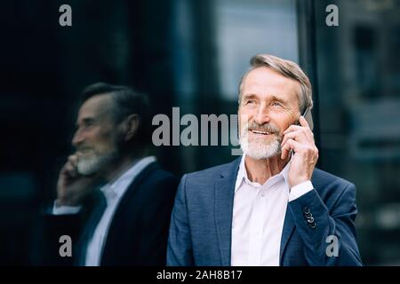 Lächelnd älterer Mann, der Anruf im Freien an einem Bürogebäude stehend Stockfoto