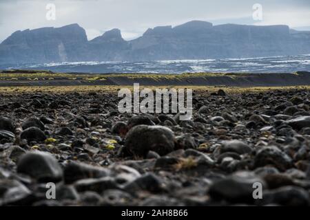 Weitwinkelansicht einer ikonischen isländischen Wüstenlandschaft mit schwarzen Felsen im Vordergrund und fernen Gletschern im Hintergrund Stockfoto