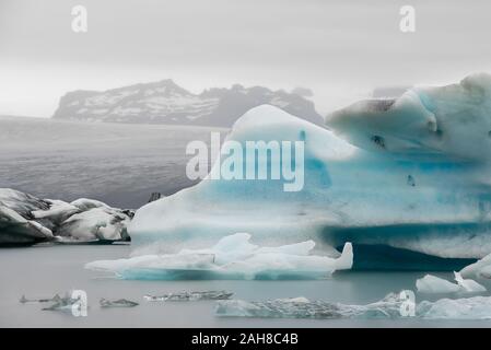 Ikonische isländische Landschaft mit einem schwimmenden Eisberg im Vordergrund und einem entfernten Gletscher im Hintergrund Stockfoto