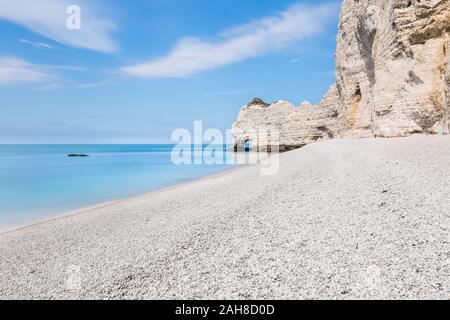 Weitwinkelansicht des Strandes von Etretat, mit weißen Kieselsteinen im Vordergrund und einer Klippe, die in einen Steinbogen im Hintergrund abfällt Stockfoto