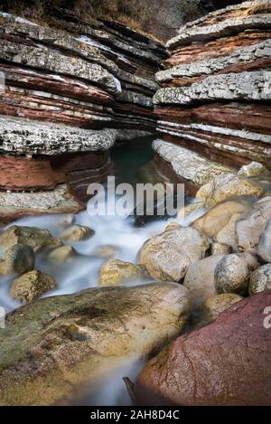 Nahaufnahme des Eingangs einer geschichteten roten Sandsteinschlucht Schlucht mit Wasser fließt auf seinem Grund in Norditalien Stockfoto