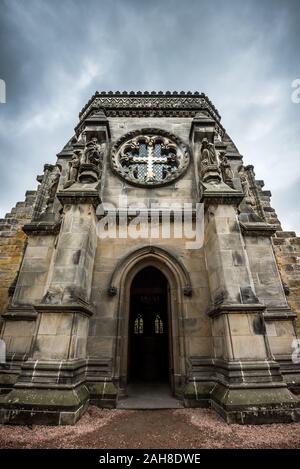 Weitwinkelansicht von unten der Fassade der schottischen Rosslyn-Kapelle, unter einem bedrohlichen grauen Himmel Stockfoto