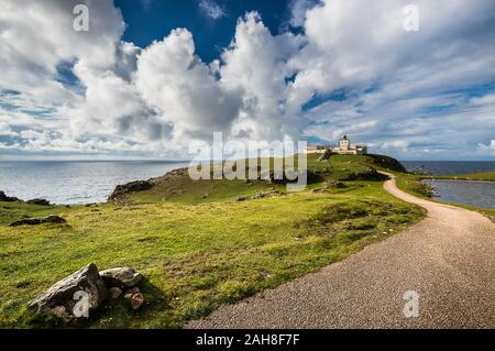 Weitwinkelansicht eines Pfades, der zu einem alten schottischen Leuchtturm führt, unter einem blauen Himmel mit dicken, puffigen Wolken Stockfoto