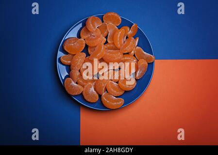 Viele Geschälte Mandarine Schichten auf den blauen Platte. Classic blau Hintergrund. Farbe des Jahres 2020, Classic Blau. Stockfoto