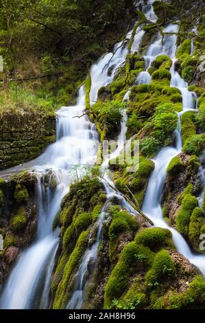 Nahaufnahme eines Bergwasserfalls, der zwischen grünen moosbedeckten Felsen fließt Stockfoto