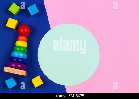 Baby Kinder Spielzeug Holz stapeln Pyramid Tower und Holz Steine in rosa und blau navy Hintergrund mit leeren runden Hellgrün Rahmen für Text oder Bild Stockfoto