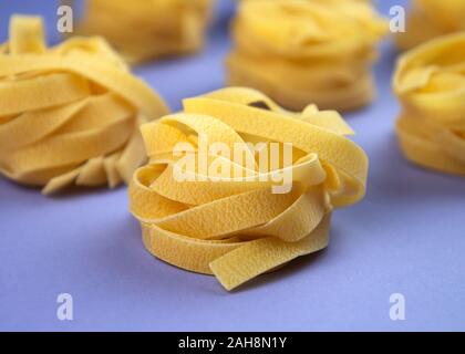 Ungekocht gerollt traditionelle italienische Pasta auf Violett Hintergrund. Teil des raw Fettuccine oder Tagliatelle oder Pappardelle. Stockfoto