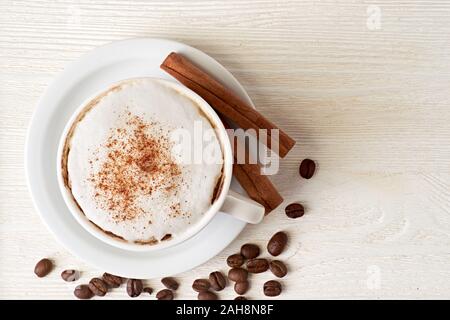 Tasse Cappuccino mit Kaffeebohnen und Zimtstangen auf Weiß Stockfoto