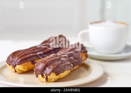 Teller mit zwei Eclairs und Tasse Kaffee auf weiße Holztisch Stockfoto