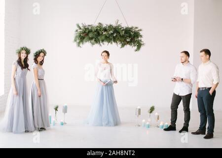 Schöne Frau Zeremonie Master in Weiß Blau Kleid stehen unter der Kiefer Bogen zusammen mit Brautjungfern und groommen vor der Trauung. W Stockfoto