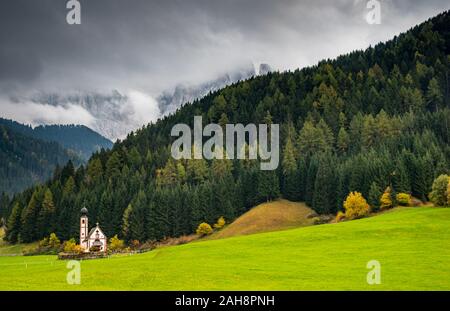 Die kleine und schöne Kirche des Heiligen Johannes, Ranui, chiesetta di San Giovanni in Ranui Runen Südtirol Italien, umgeben von grünen Wiesen, Wald ein Stockfoto