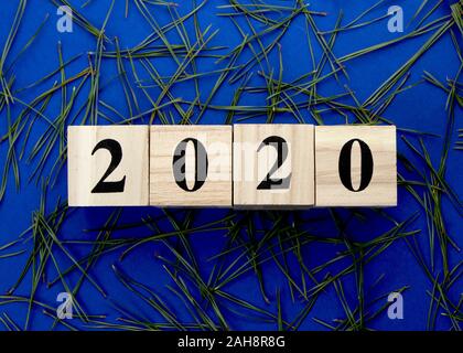 Holzwürfel mit der Inschrift 2020 auf einem blauen Hintergrund mit Tannennadeln. Stockfoto