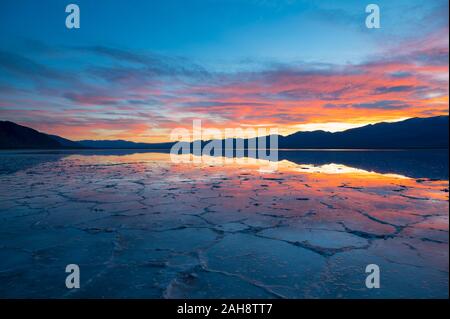 Farbenfroher Sonnenuntergang über einem überfluteten Badwater Basin im Death Valley National Park mit Spiegelungen der Berge im Wasser in Kalifornien am 14. Dez. 2019 Stockfoto