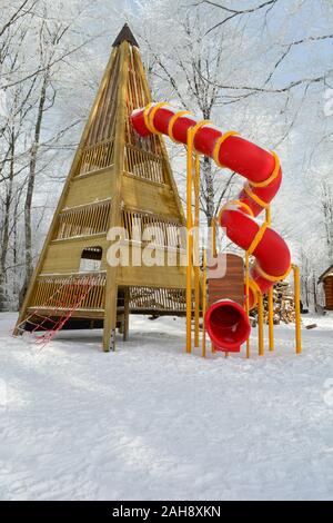 Große Rodelbahn mit Holz- pyramidenförmigen Sockel und Rot twisted Rohr auf verschneiten Spielplatz mitten im Wald, Mountain Ski Resort Stockfoto