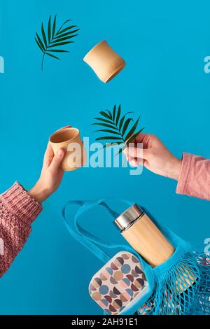 Null Abfall Kaffee in umweltfreundliche isolierte Bambus Kolben. Zwei Hände mit Schale und Palm Leaf, Netztasche mit Mittagessen und Kaffee Kolben fliegen. Null Abfall Stockfoto