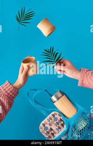 Null Abfall Kaffee in umweltfreundliche isolierte Bambus Kolben. Zwei Hände mit Schale und Palm Leaf, Netztasche mit Mittagessen und Kaffee Kolben fliegen. Null Abfall Stockfoto