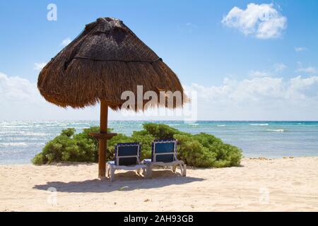 Zwei Stühlen unter einem Sonnenschirm im Schatten an einem Strand in den Tropen. Stockfoto
