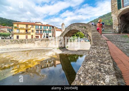 Touristen, darunter eine attraktive jüngere Paare, Sehenswürdigkeiten in der Nähe der Monet Bogenbrücke der mittelalterlichen Dolceacqua, Italien.