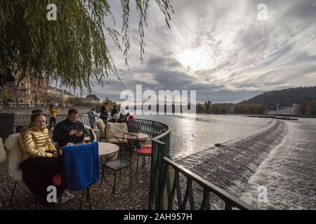 Prag, Tschechien - NOVEMBER 2, 2019: Zwei Touristen, Liebhaber, entspannend und sitzen in einem Café, das Panorama der Prager vom Flussufer des Mol Stockfoto